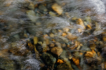 Rocky bottom of mountain river through the clear water, selective focus, blurring the image. Cristal water in the stream shimmers in sunlight. Stone background.