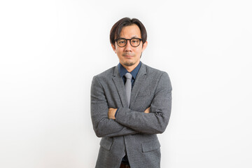 Confident Asian businessman in grey suit and eyeglasses posing with arms crossed standing over white wall background, Business success concept.