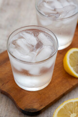Fresh Lemon Sparkling Water with Ice on a rustic wooden board, low angle view. Close-up.
