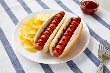 Tasty American Hot Dog with Potato Chips on a white plate, low angle view.