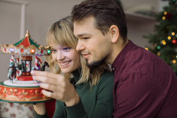 Happy couple in love looking at musical toy Christmas carousel. Christmas holidays at home.
