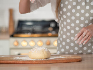 Knead dough, hand dough and flour close-up. A pastry chef in a grey polka-dot apron.