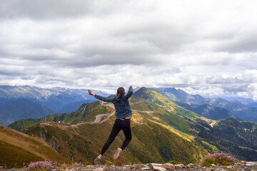 Fototapeta premium A young female tourist on top of a mountain jumps into the sky. Happiness and a sense of freedom,