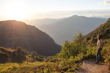 Fototapeta premium Young woman admire the landscape in the mountains. Golden rays of the evening sun