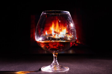 Close-up on a glass of brandy in the dark on the background of the fireplace