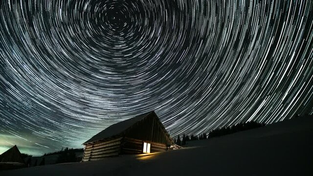 Wooden house in the mountains in winter. Stars move around a polar star. Time lapse of Star trails in the night sky. 4K
