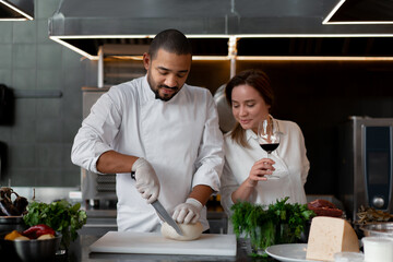 Handsome young African chef is cooking together with his Caucasian girlfriend in the kitchen using red wine as an ingredient.