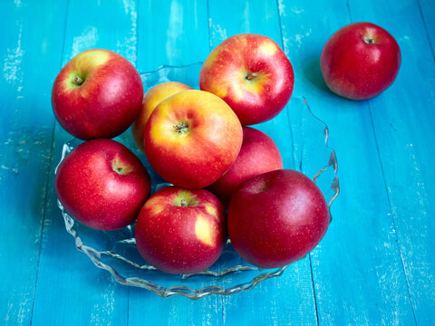 Bright red and yellow apples in a vase on a blue background.