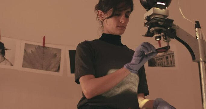 Female photographer developing film and printing photographs in traditional process in darkroom. Portrait of creative girl photographer in photo studio darkroom. Developing analog camera film.