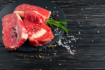 Three pieces of juicy raw beef on a stone cutting board on a black wooden table background.