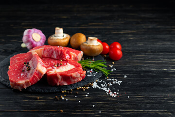 Three pieces of juicy raw beef on a stone cutting board on a black wooden table background.