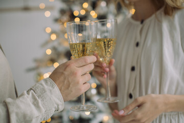 Couple making a celebratory toast with glasses of champagne against Christmas lights at home. Family holiday moments concept.