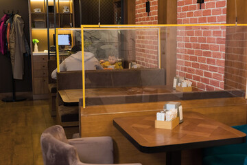 The family eats in a cafe with transparent fences between the tables. The concept of social distancing, security in a pandemic.
