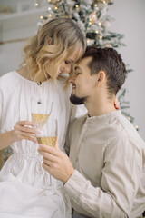 Happy young couple toasting with glasses of champagne while celebrating Christmas. Light colors.