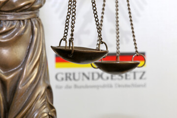 Nahaufnahme einer Justitia vor dem deutschen Grundgesetzbuch