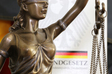 Nahaufnahme einer Justitia vor dem deutschen Grundgesetzbuch