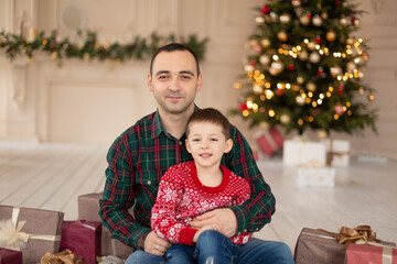 Obraz na płótnie Canvas Smiling father hug his son at Christmas tree, surrrounded presents. Happy family holidays.
