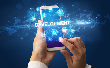 Female hand holding smartphone with DEVELOPMENT inscription, modern technology concept