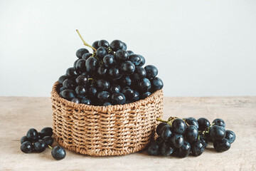 Bunch of black grapes in a round wicker basket on a old wooden table. Copy, empty space for text