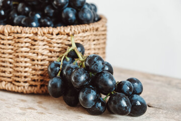 Bunch of black grapes in a round wicker basket on a old wooden table. Copy, empty space for text