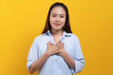 Appreciated expression. Pleased asian woman keeping hands on chest and smile isolated on yellow...