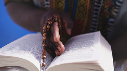 Unrecognizable African black man in traditional dress with rosary reading the Holy Bible . High quality photo