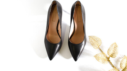 Classical black shoes. High heel shoes on white background. Front view picture. Gold brunch with leaves. Space for text. Element for design.