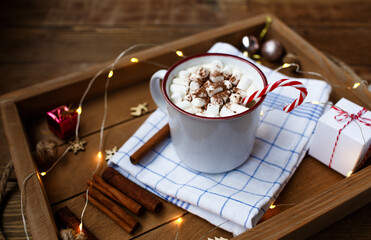 a Cup of hot Christmas drink on a wooden background around a cinnamon stick and Christmas gifts