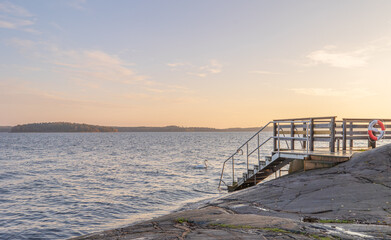 Bathing jetty with stairs to Baltic sea and swan in Stockholm Sweden in stunning sunrise with rocks in beautiful light