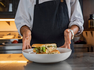 Closeup image of a female chef cooking and holding a piece of whole wheat sandwich in kitchen