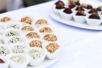 healthy sweets of grated nuts and dried fruits. vegetarian energy ball candies in white craft paper in glass plate stand on white table in the morning on holiday.  Selective focus