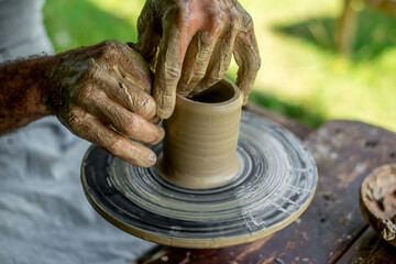 Hands of a potter shaping a clay pot on a potter wheel
