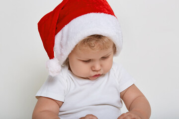 Cute baby wearing christmas clothes playing indoor, looking attentively at something in his hands, has blond wavy hair, has concentrated look, posing isolated over white background.