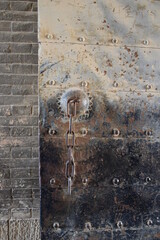 Ancient, rusty, and dusty iron gate with metal chain with brick wall backdrop, Qinghai, China