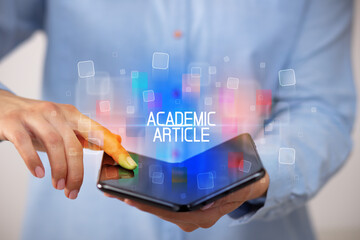 Young man holding a foldable smartphone with ACADEMIC ARTICLE inscription, educational concept
