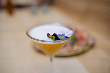 Purple flowers on a frothy cocktail with a blurry pizza as background
