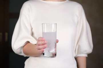 woman holds glass of water with effervescent tablet of aspirin