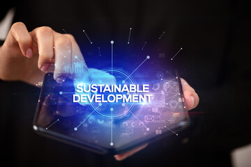 Businessman holding a foldable smartphone with SUSTAINABLE DEVELOPMENT inscription, new business concept