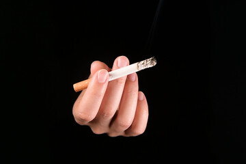 A hand with a smoking cigarette emerges from the darkness, inviting the viewer to smoke. Tobacco addiction hazard concept