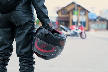 A motorcyclist in leather pants with a helmet in his hands stand to the motorcycle in the parking...
