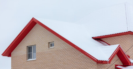 White snow lies on the red roof of the house.