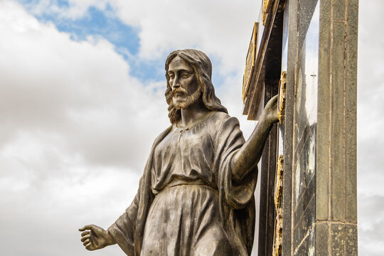 Escultura simbolizando Jesus Cristo em topo de mausoléu dentro de um cemitério.