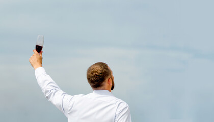 office employee man in a white shirt with a glass of wine in a raised hand against the sky