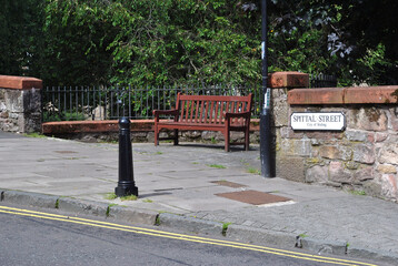 Empty Wooden Public Bench beside Stone Wall & Road with Iron Bollard  