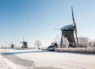 Three windmills in the winter near rozen canal in winterlandscape with snow and ice