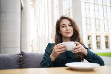 portrait of a woman of European appearance, brunette, long hair, resting in a summer cafe. business woman drinks coffee break drinks a full-bodied tea.
