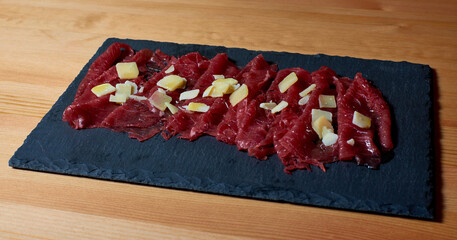 Veal carpaccio with parmesan cheese presented on a slate plate.