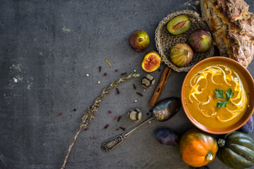 Autumn menu. Top view photo of bowl with pumpkin soup, gem squashes, rosemary, pepper, fresh baked bread and silver spoon. Dark grey textured background. Healthy eating concept. 
