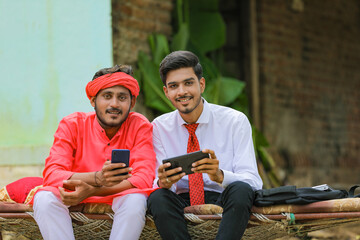 Fototapeta premium Young indian agronomist or banker showing some information to farmer in smartphone