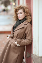 Portrait of a young woman with curly hair outdoors. Girl standing leaning against the wall